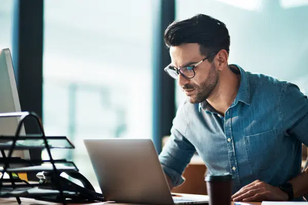 Person with glasses sitting behind the table with a laptop, looking into the laptop.