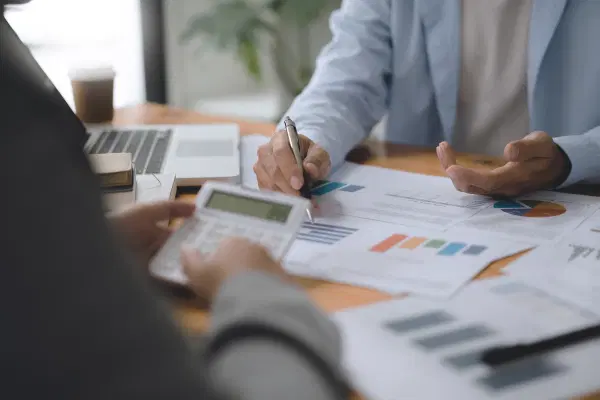 Two people sitting behind the table with a calculator and discussing over the chart printouts.