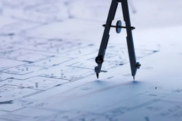 Compass standing on top of a blueprint of a floor plan.