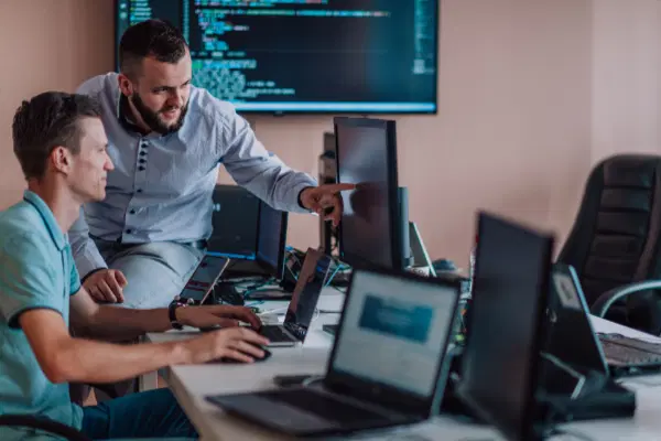 Two people in a computer lab discussing the problem and pointing to a screen.