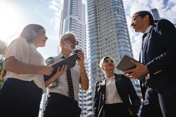 Four people standing near the high-rise office building and discussing details of the implementation project phase.